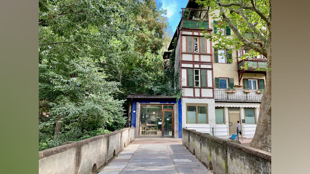 A blue building with a brown roof is in front of a green tree.