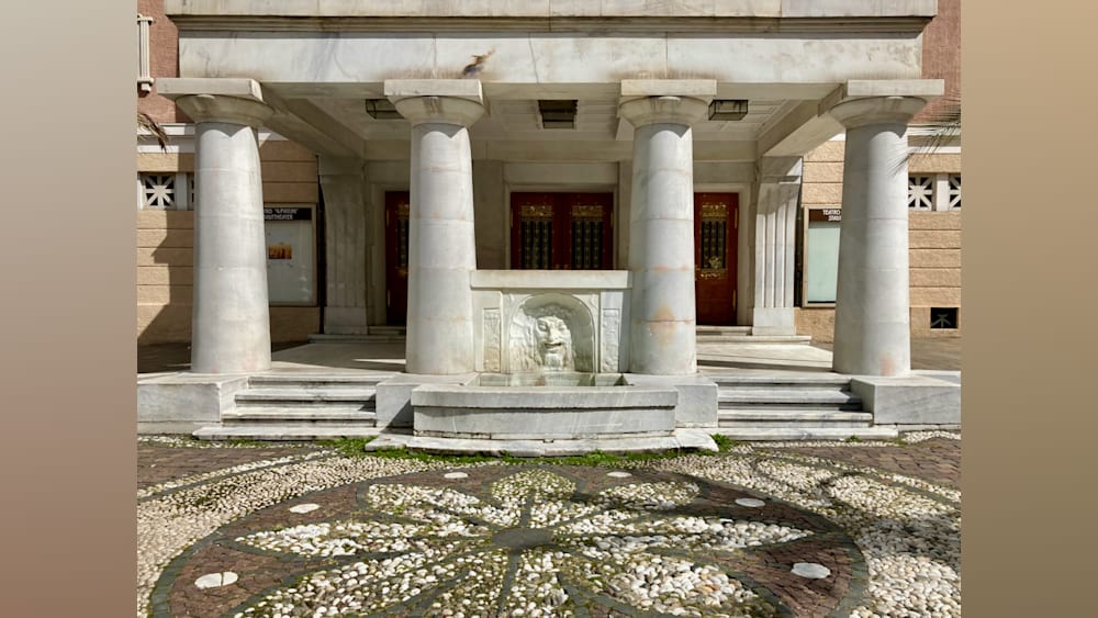 A building with a fountain in the middle of the walkway with steps leading up to it.