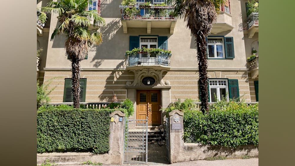 A large, cream-colored building with a gate and a balcony on the second floor.