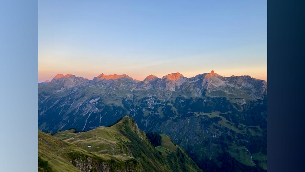 A mountain with a valley in between with the sun setting in the background.