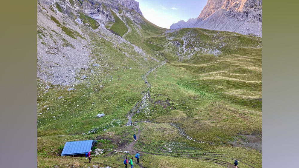 Several people walking up a hill with a blue roof in the background.