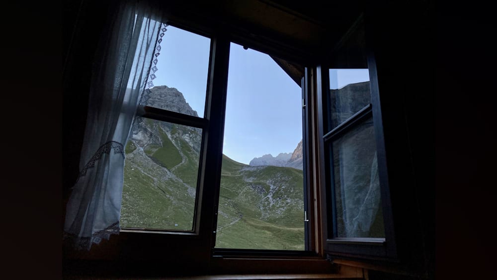 An outside view of a green mountainside through an open window.