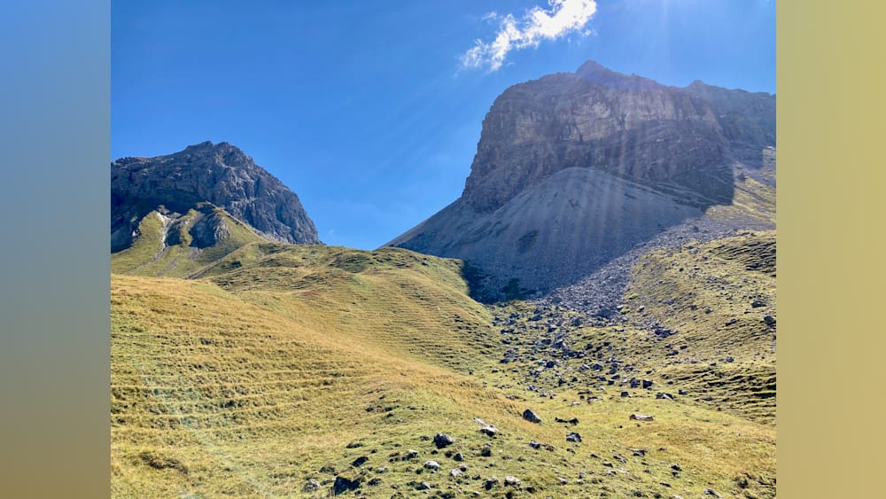 A mountain with a grassy slope is shown with the sun shining on it.