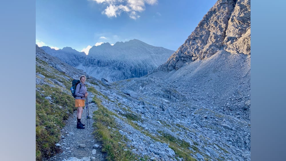 A woman standing on a mountain with a backpack and hiking poles.