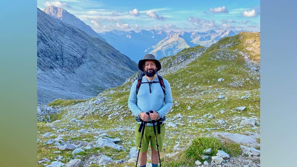 A man standing on a mountain with his hiking poles and a backpack.
