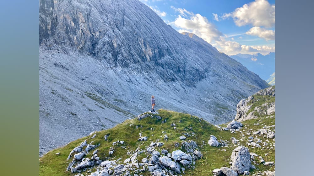 A woman standing on a hillside with a dog at her feet.