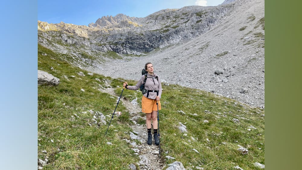 A woman standing on a mountain with her hiking poles and backpack on.