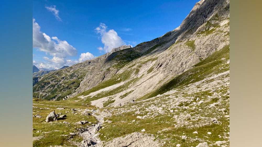 A large mountain with a path going down to the valley with some people walking on the path.