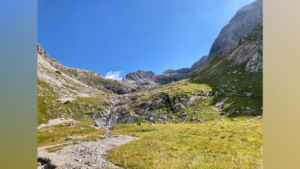 A view of a mountain and valley with grass and rocks.