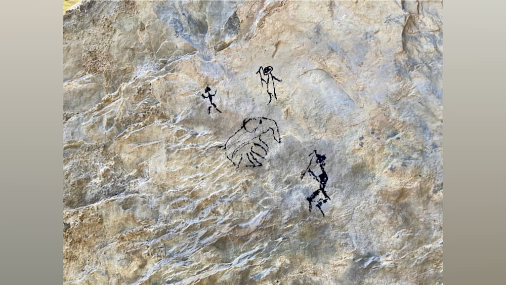 Paleolithic drawing on a rocky wall with people and animals depicted.