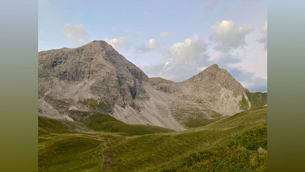 A mountain with a path going up and a field with grass.