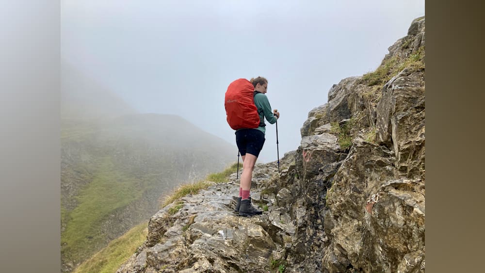 A woman with a red back pack looking at a mountain.