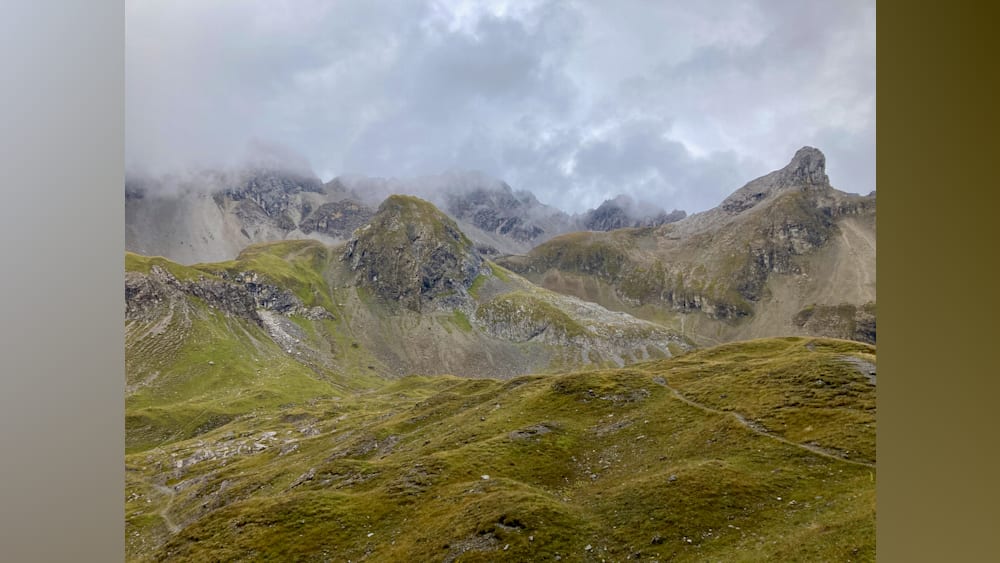 A foggy mountain peak with a grassy slope underneath.
