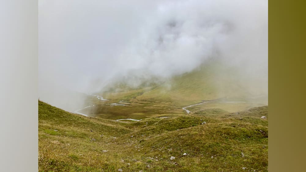 A foggy mountain landscape with a stream running down the side.