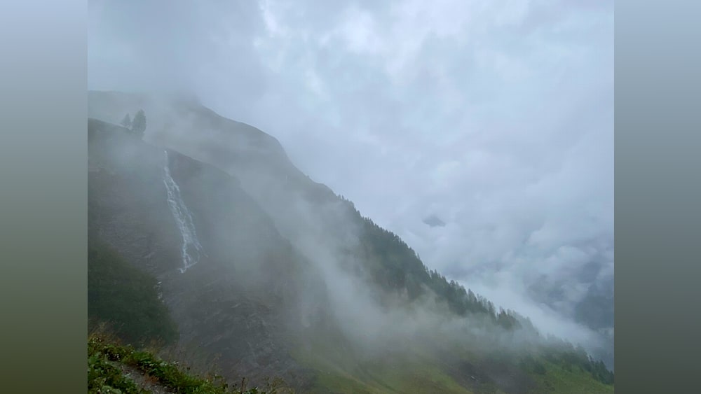 A mountain with a waterfall and a lot of misty clouds.