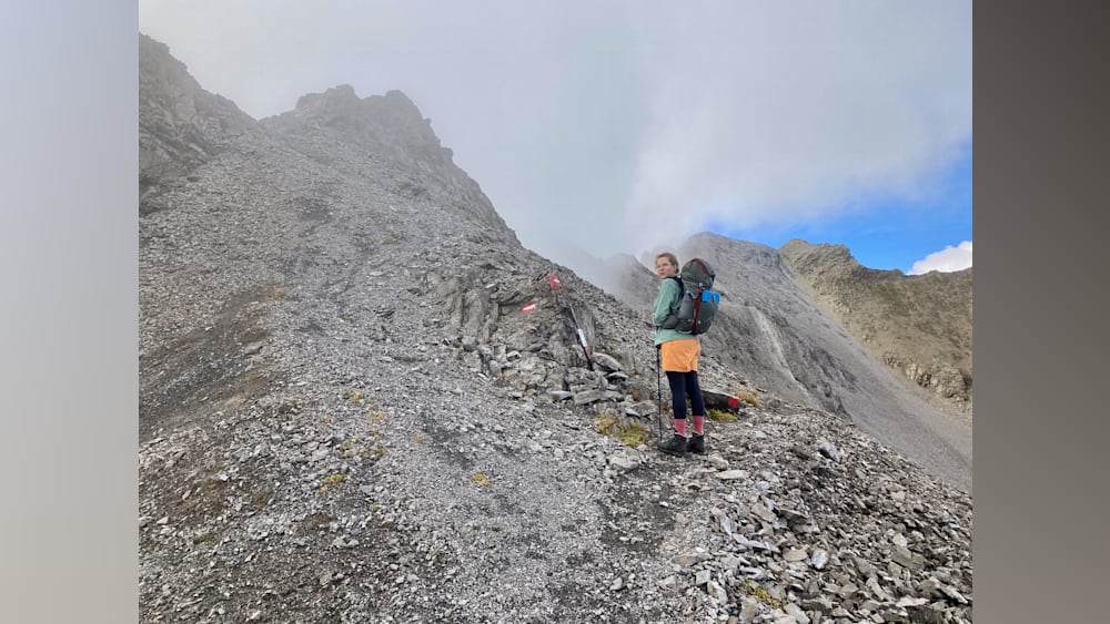 A woman standing on a mountain with a backpack on her.
