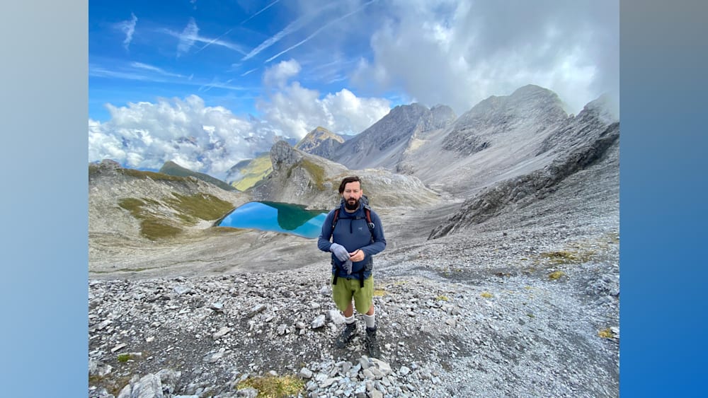 A man standing on a mountain with a blue lake in the background.