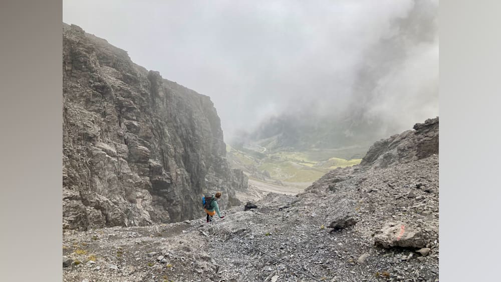 A man with a blue backpack is climbing up a rocky mountain pass.