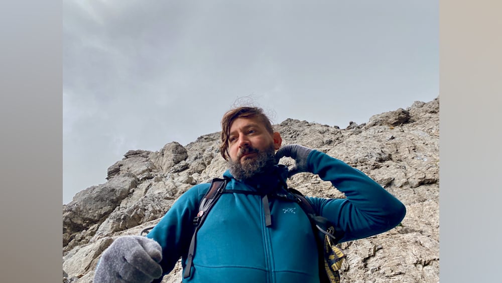 A man wearing a blue jacket with a black backpack on a mountain.