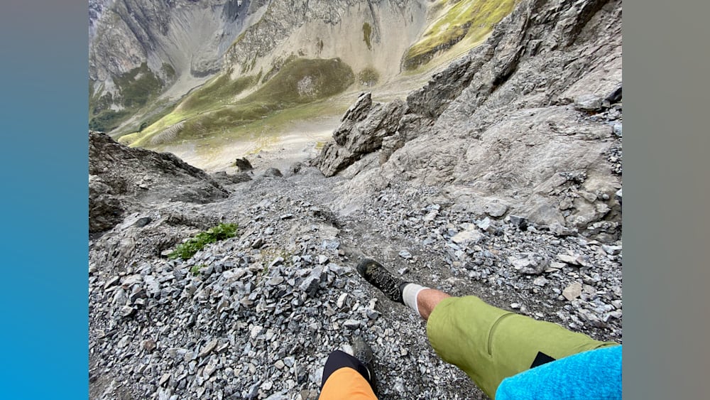 A man and woman are hiking up a rocky mountain side in their shorts and shoes.