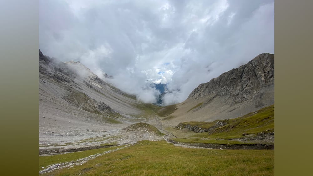 A valley with a lot of grass and a lot of clouds in it.
