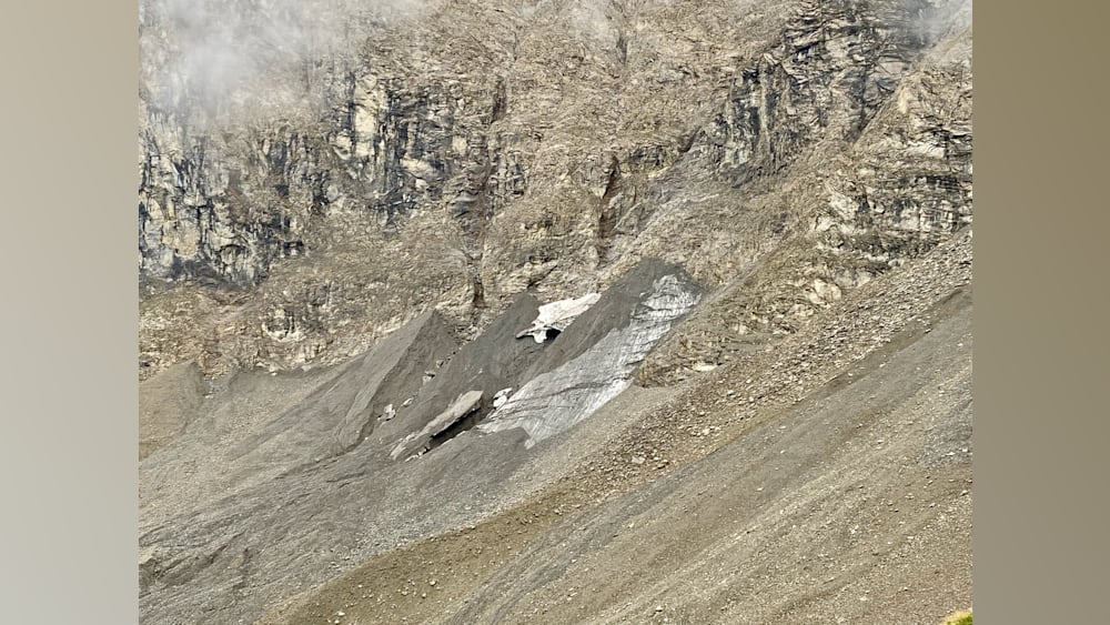 A large grey boulder is sitting on a hillside with some dirt and rocks around it.