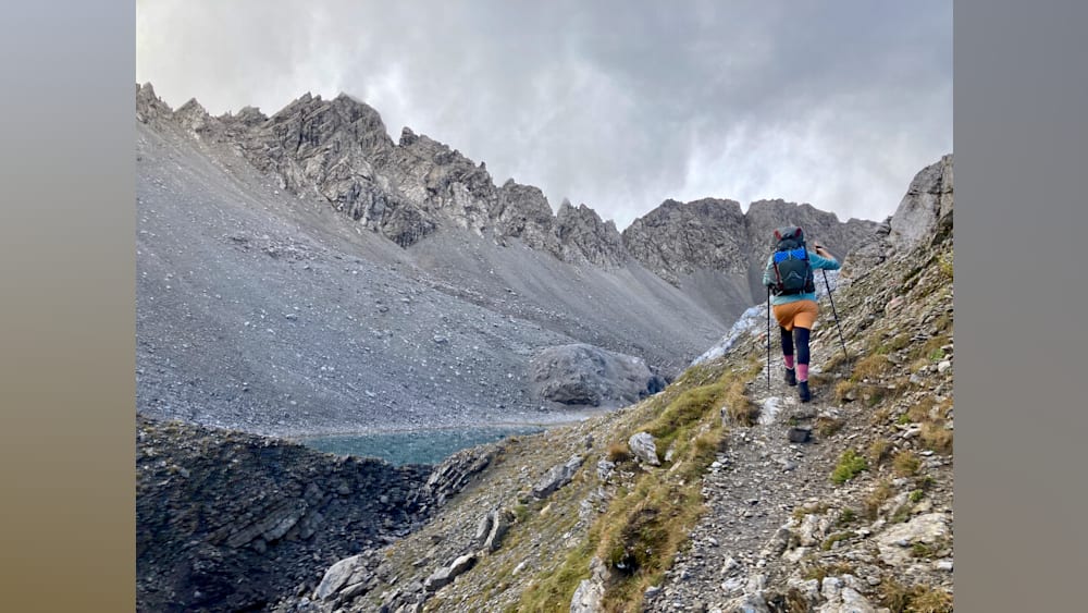 A woman hiking up a mountain with a blue lake in the background.