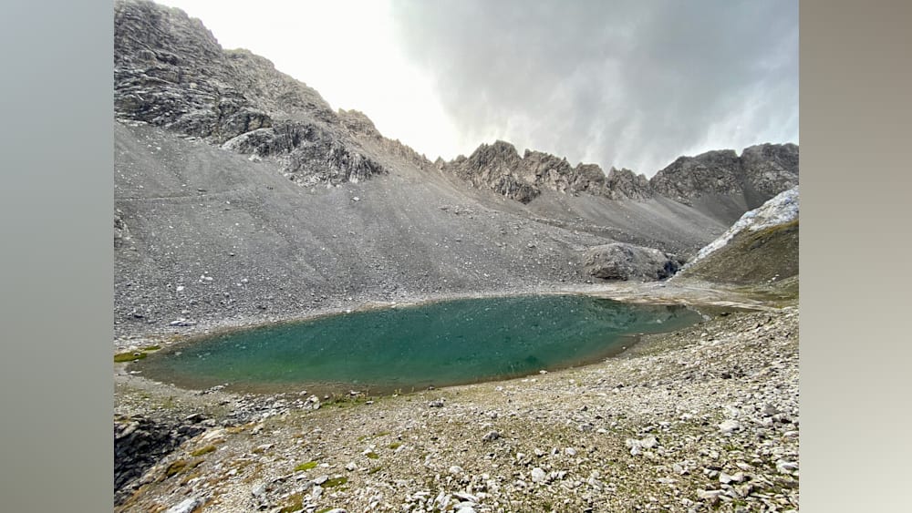 A large lake surrounded by mountains is reflected in the sky.