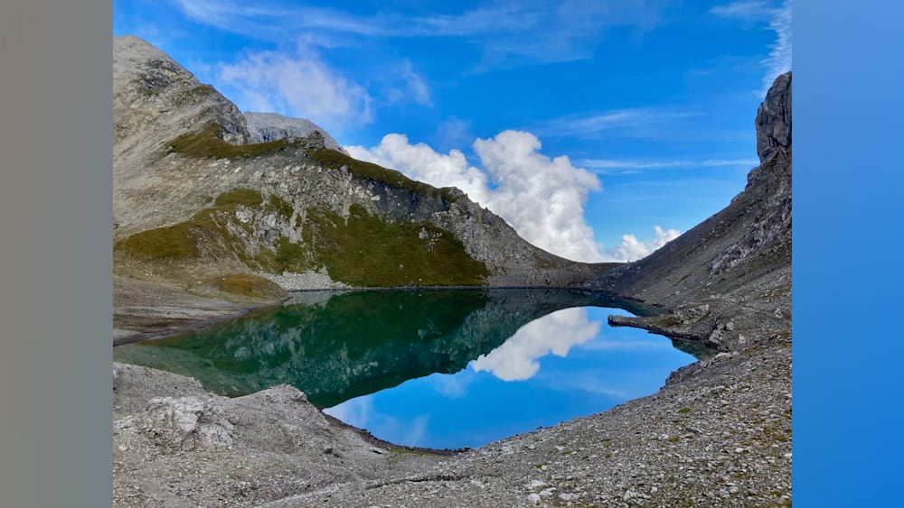 A large lake surrounded by mountains is shown with a reflection in the water.