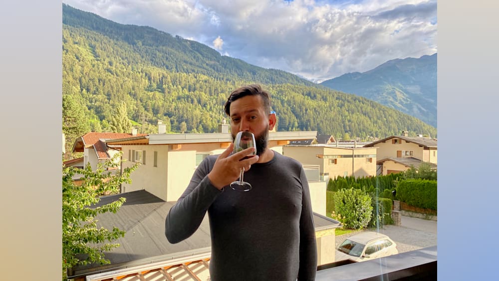 A man in a grey shirt is drinking from a wine glass.