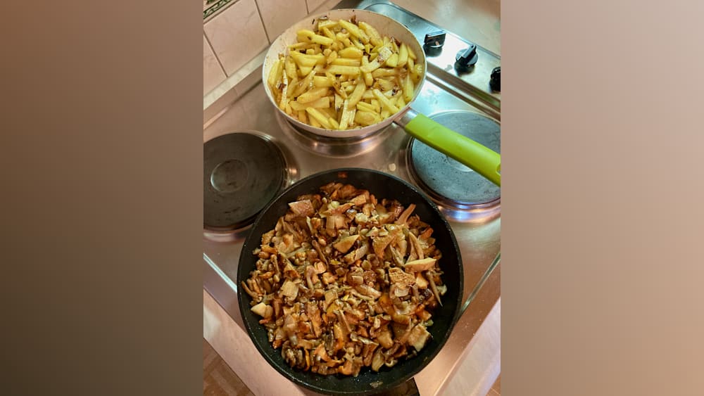 pans full of food on a stove with one pan containing mushrooms and another containing fried potatoes.