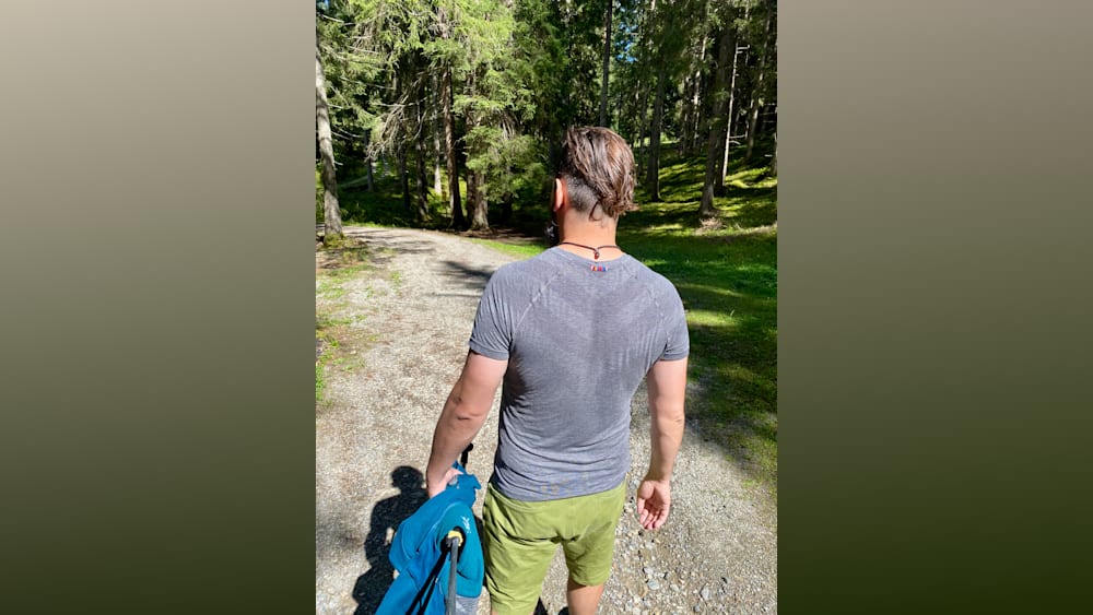 A man walks down a path with his arm behind him holding a blue object.