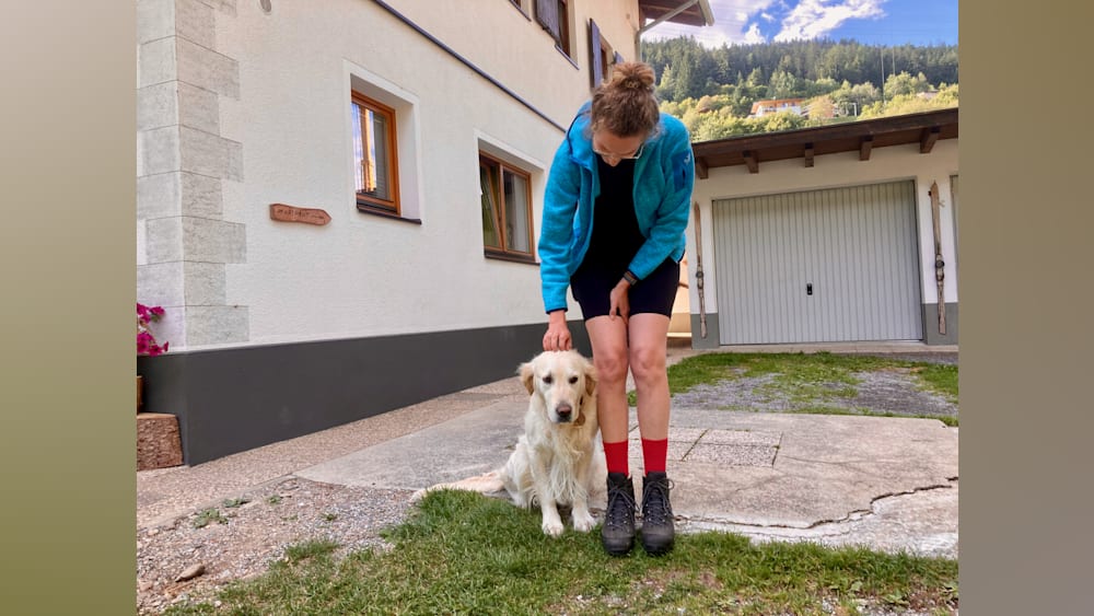 A woman petting her dog while wearing shorts and a blue jacket.