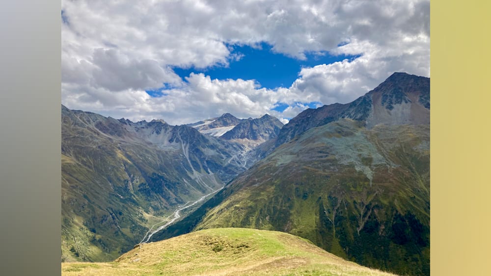 A mountain with a valley and a cloud covered mountain in the distance.