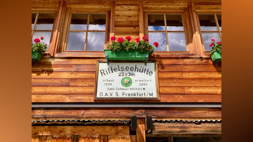 A sign that says "Rffselsehutte" on the side of a building with flowers in a planter next to it.