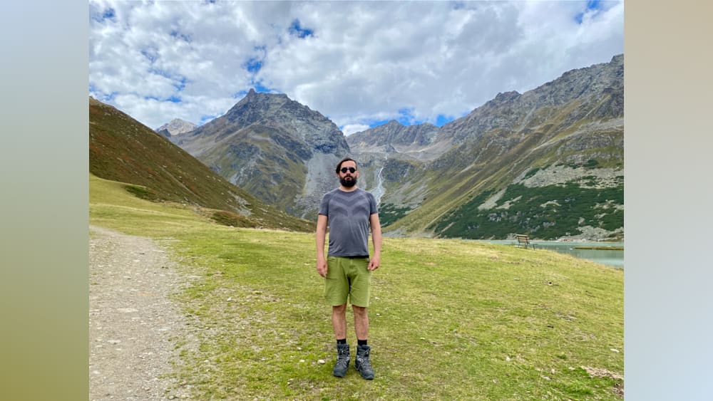 A man stands in a field with mountains in the background.