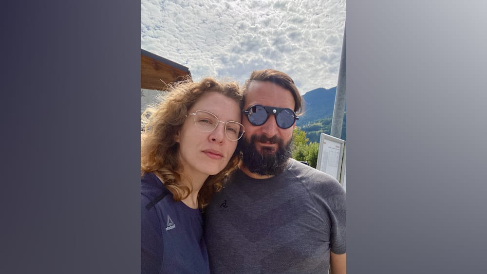 A woman with a gray framed face poses with a man wearing black sunglasses.