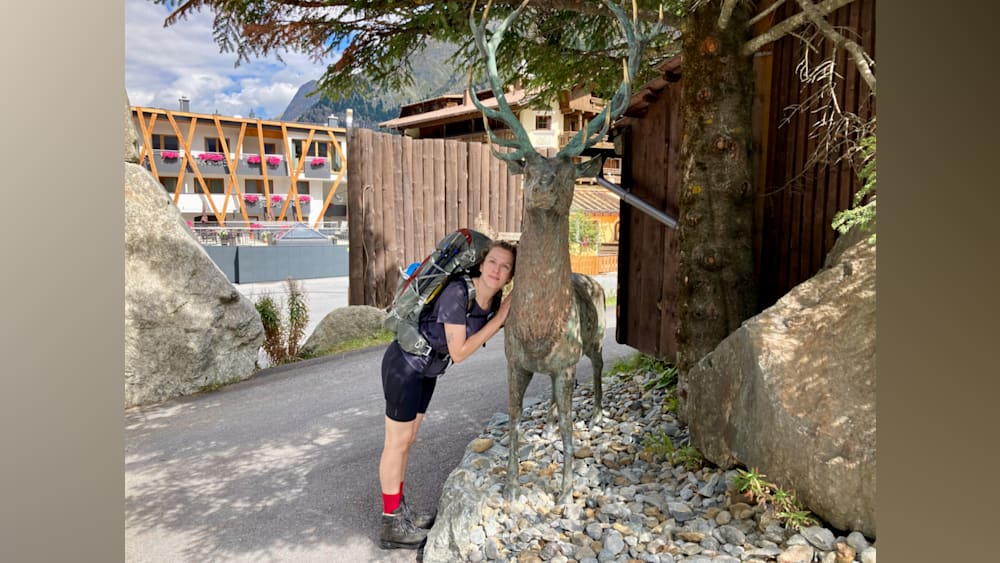 A woman leaning on a deer statue with a backpack on her shoulders.