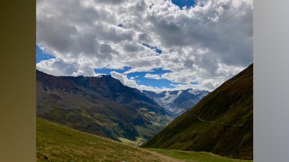 A mountain with a valley and a cloud covered mountain in the distance.