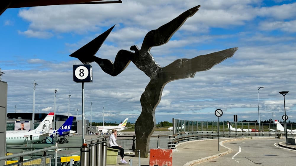 A woman sitting on a bench next to a large metal sculpture of a bird.
