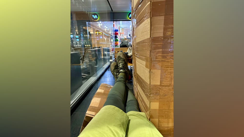 A person in a green shirt is sitting next to a wall of cardboard boxes.