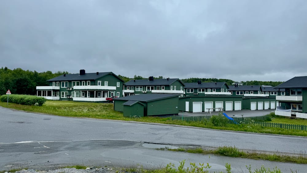 A road with green houses and a red car parked in front of one of them.