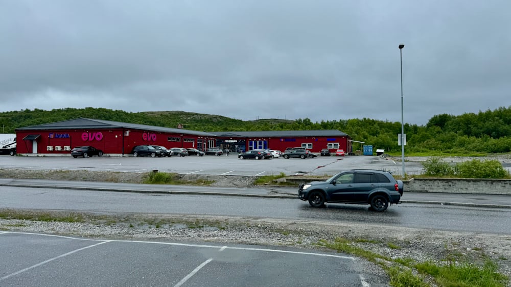 A black car is driving down a street next to a red building.