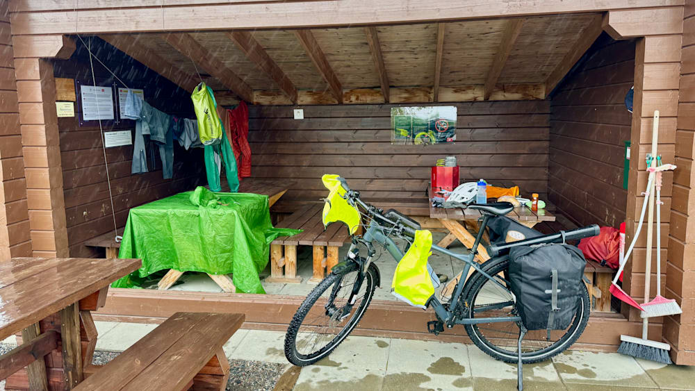 A bicycle is parked next to a table outside with an umbrella and a jacket draped over it.