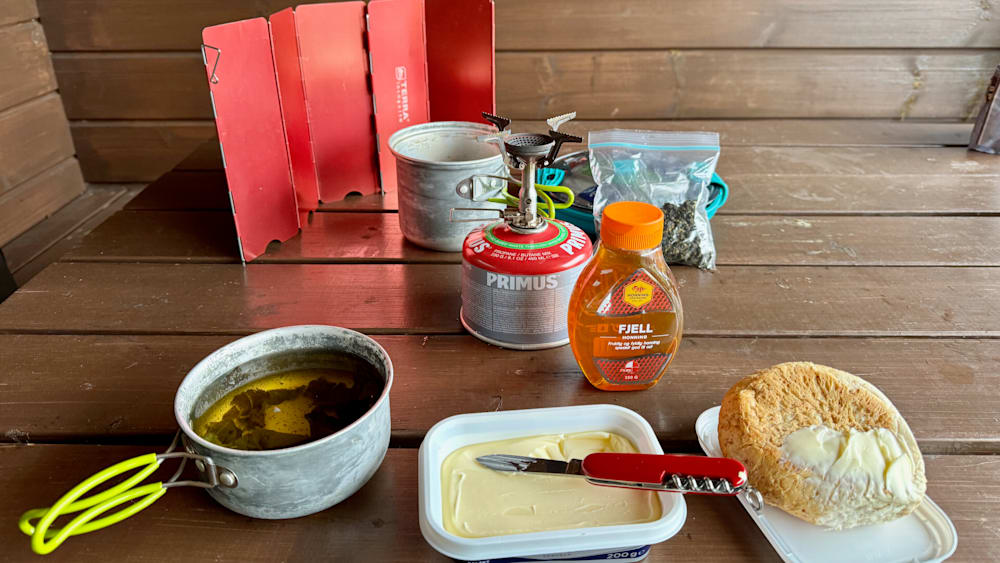 Primus gas canister and utensils are on a table next to containers of food.
