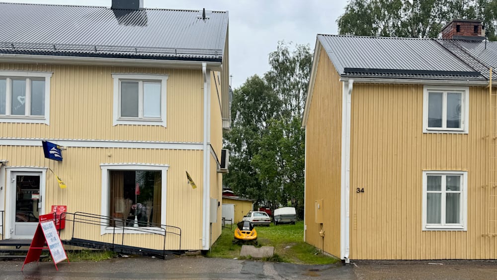 A yellow house has a black and white flag on it and a snowmobile parked in front.