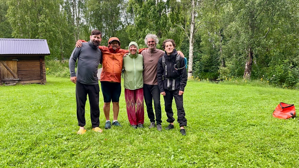 Five people posing for a picture in a field, two of them wearing raincoats.