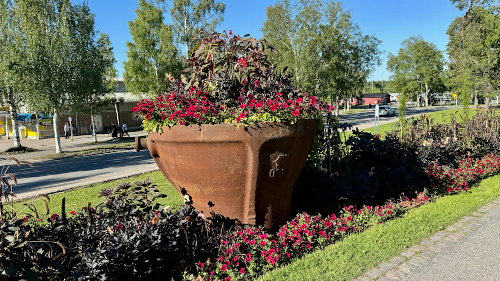 A large flower pot is in front of a building with a sidewalk in front of it.