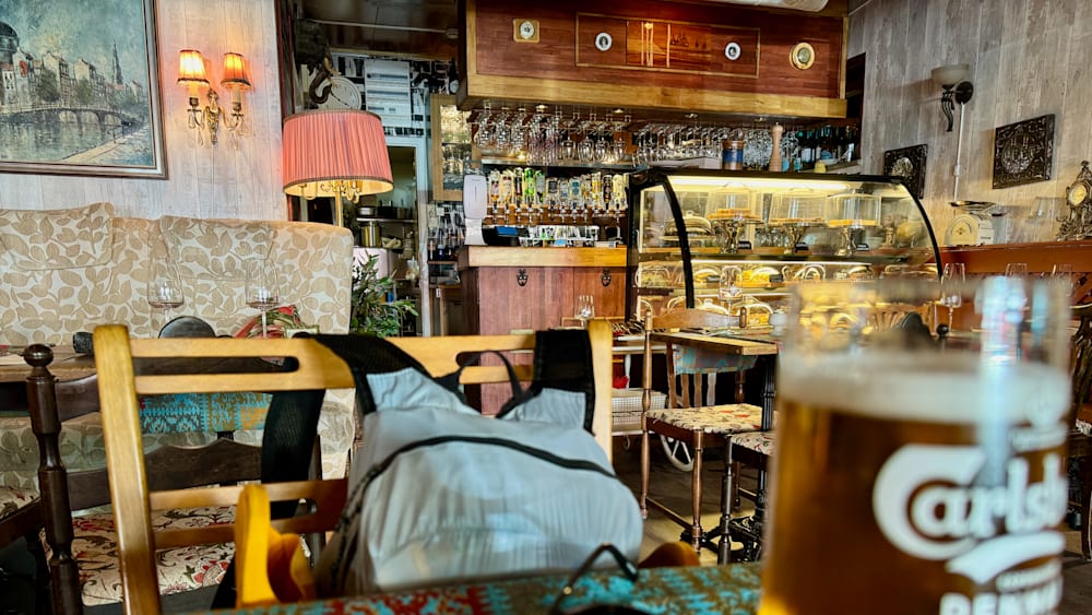 A bag sitting on a chair at a restaurant with a glass of beer next to it.