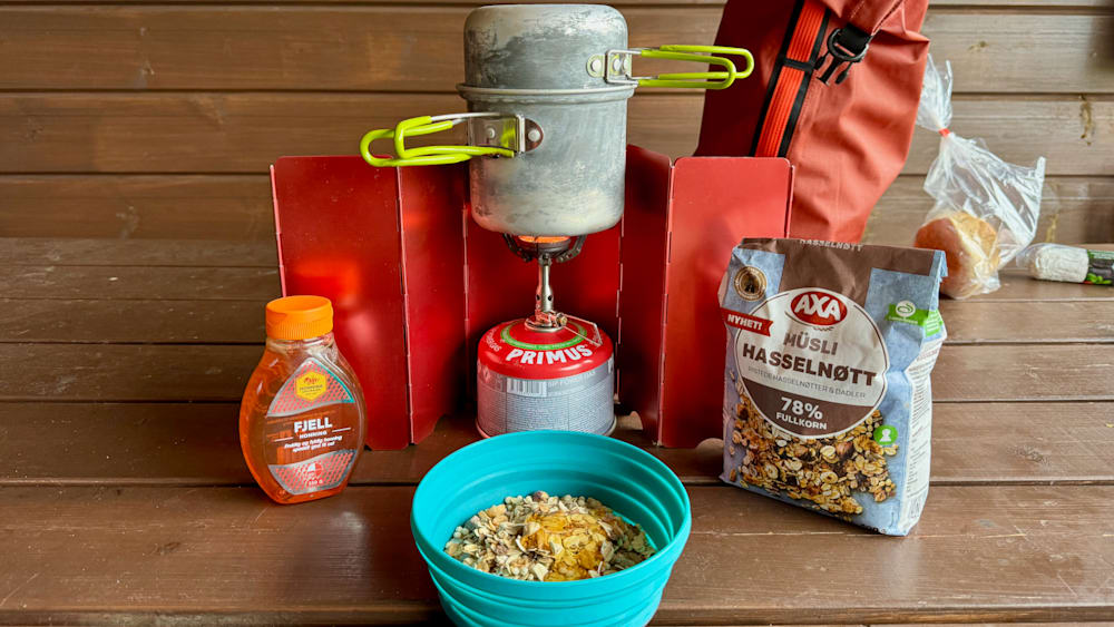 A camping stove with a blue bowl of cereal next to a bag of primesuts.